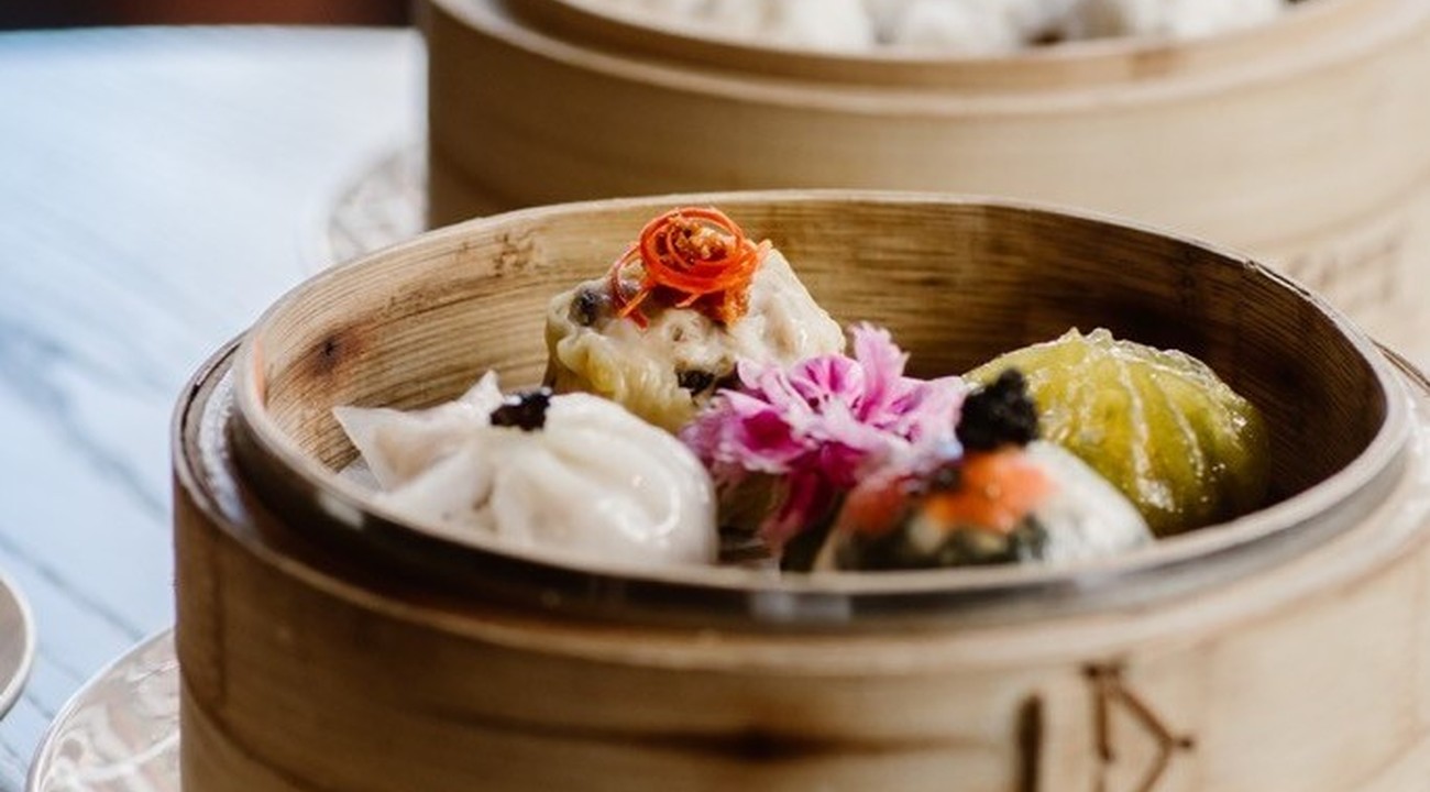 Bamboo steamer baskets containing colorful gourmet dim sum with decorative garnishes on white plate