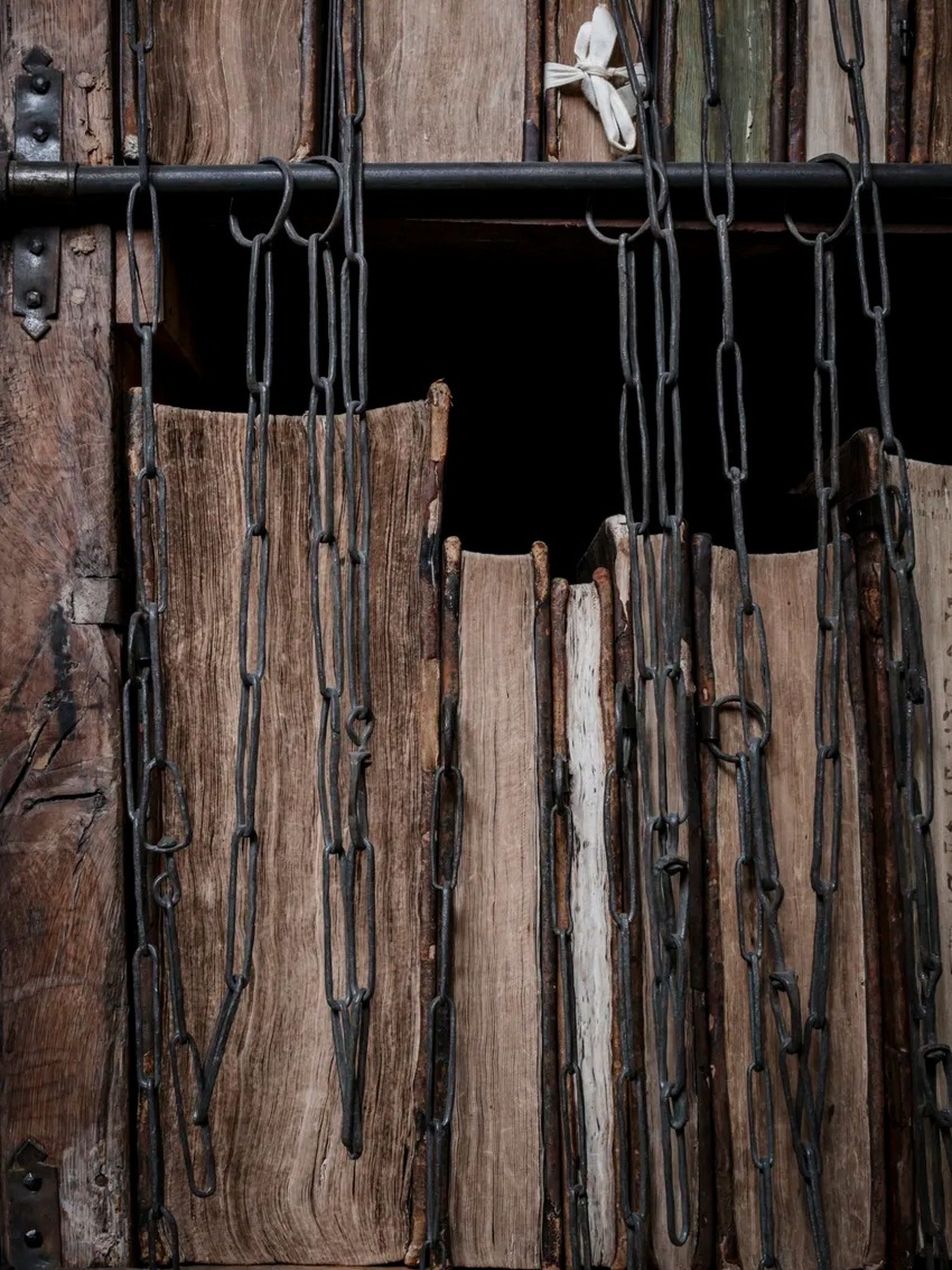 Weathered medieval chained books with iron links hanging from a rod on wooden shelving.