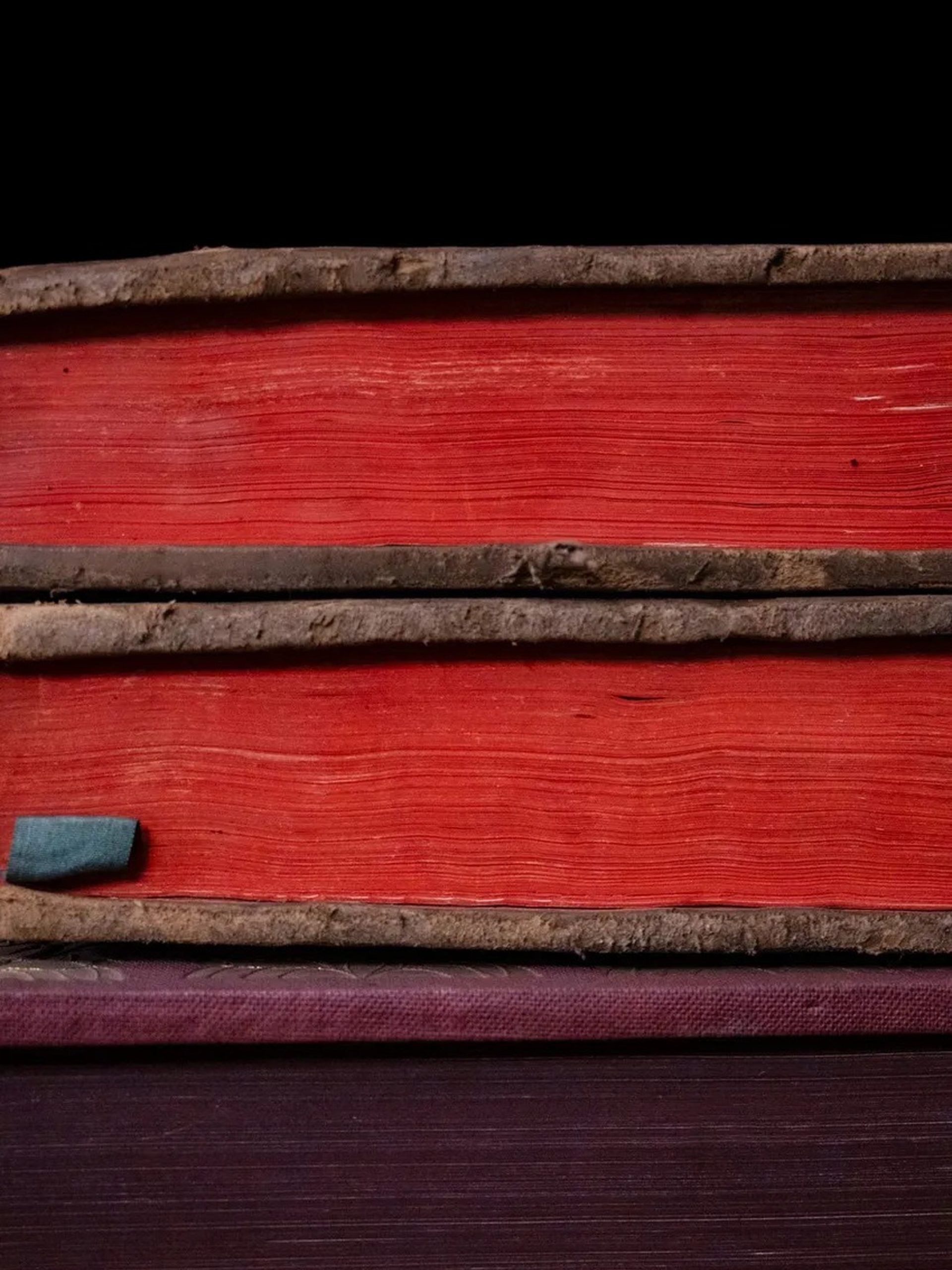 Close-up of three stacked antique books with red and purple fore-edges and worn leather spines.