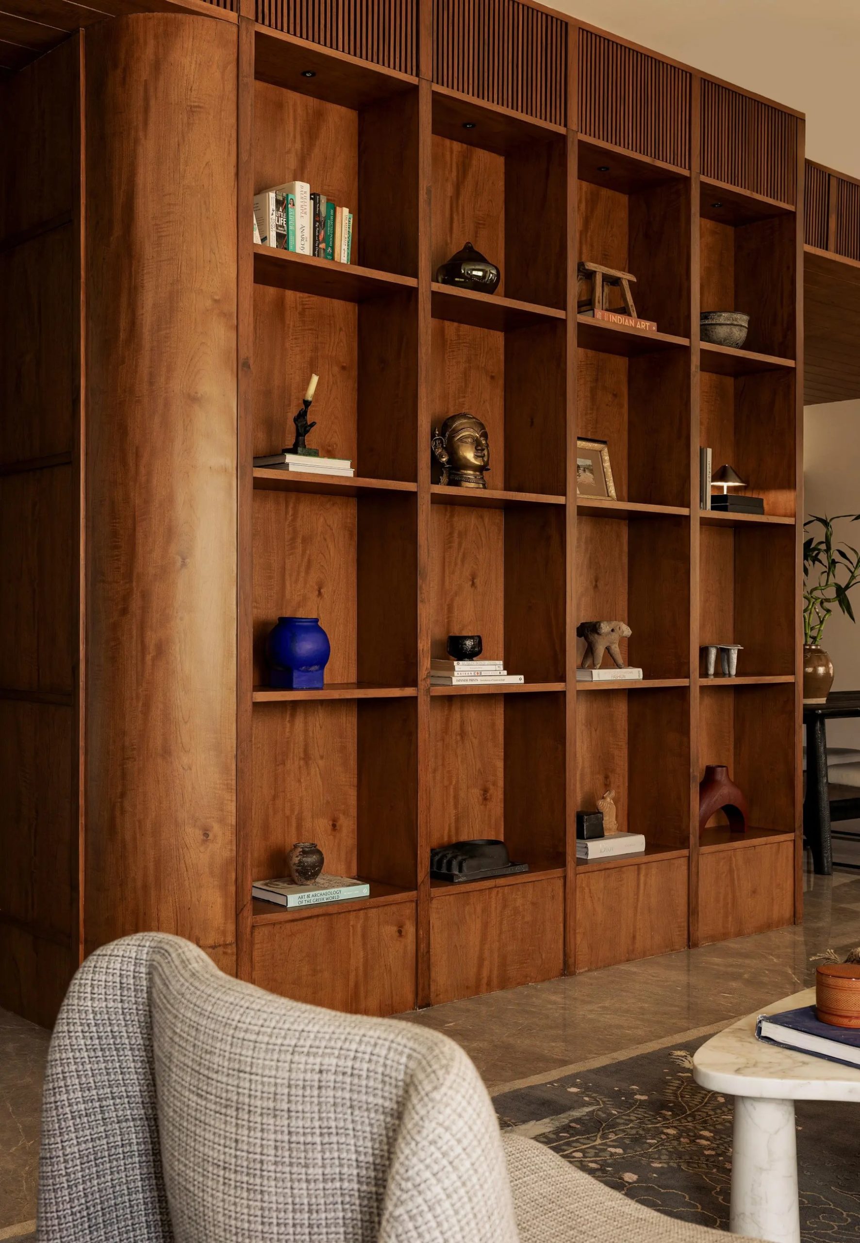 Floor-to-ceiling walnut bookshelf styled with sculptures, art books, and a cobalt blue vase.