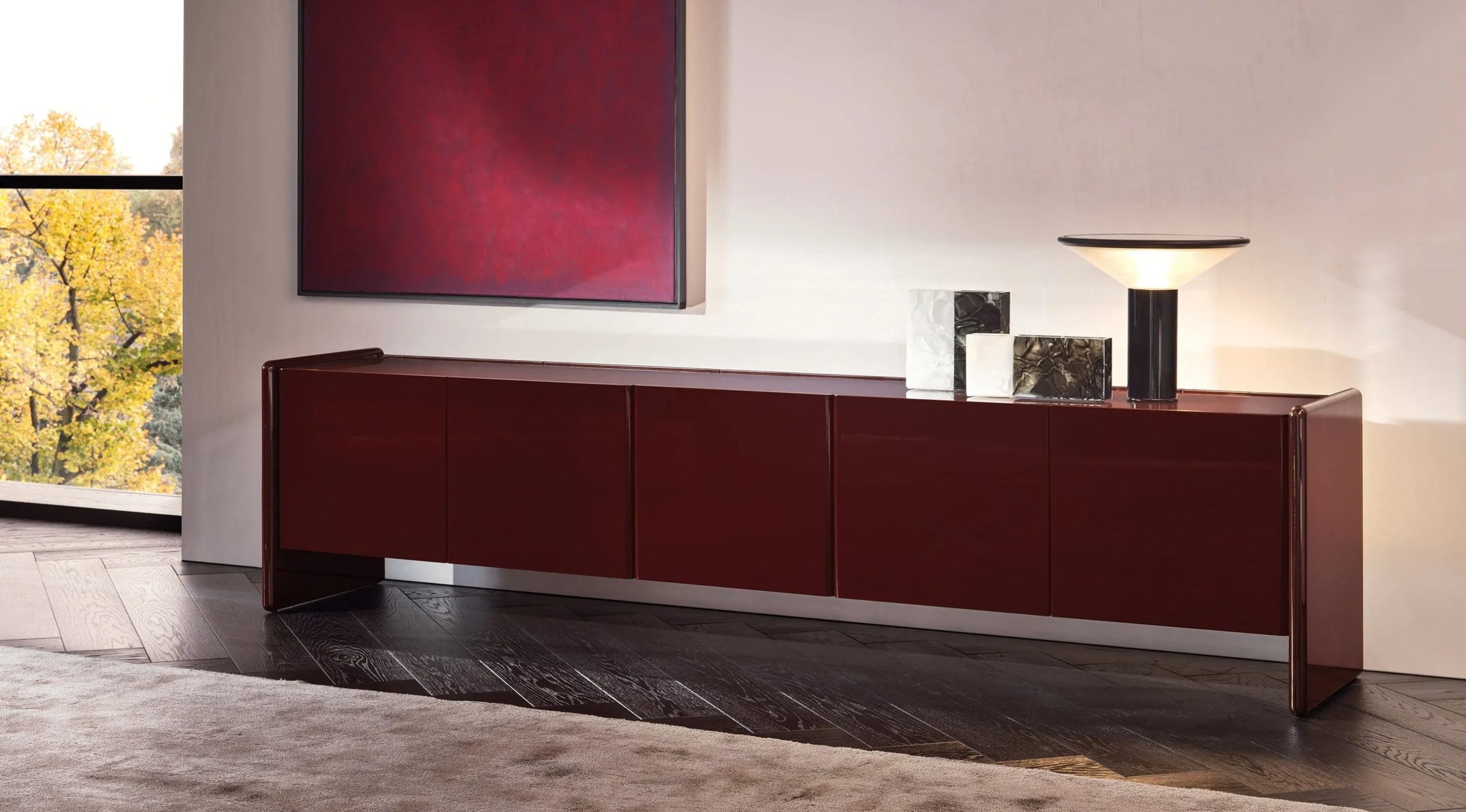 Deep burgundy lacquered sideboard with marble decorative objects and a minimalist table lamp in a luxury interior.