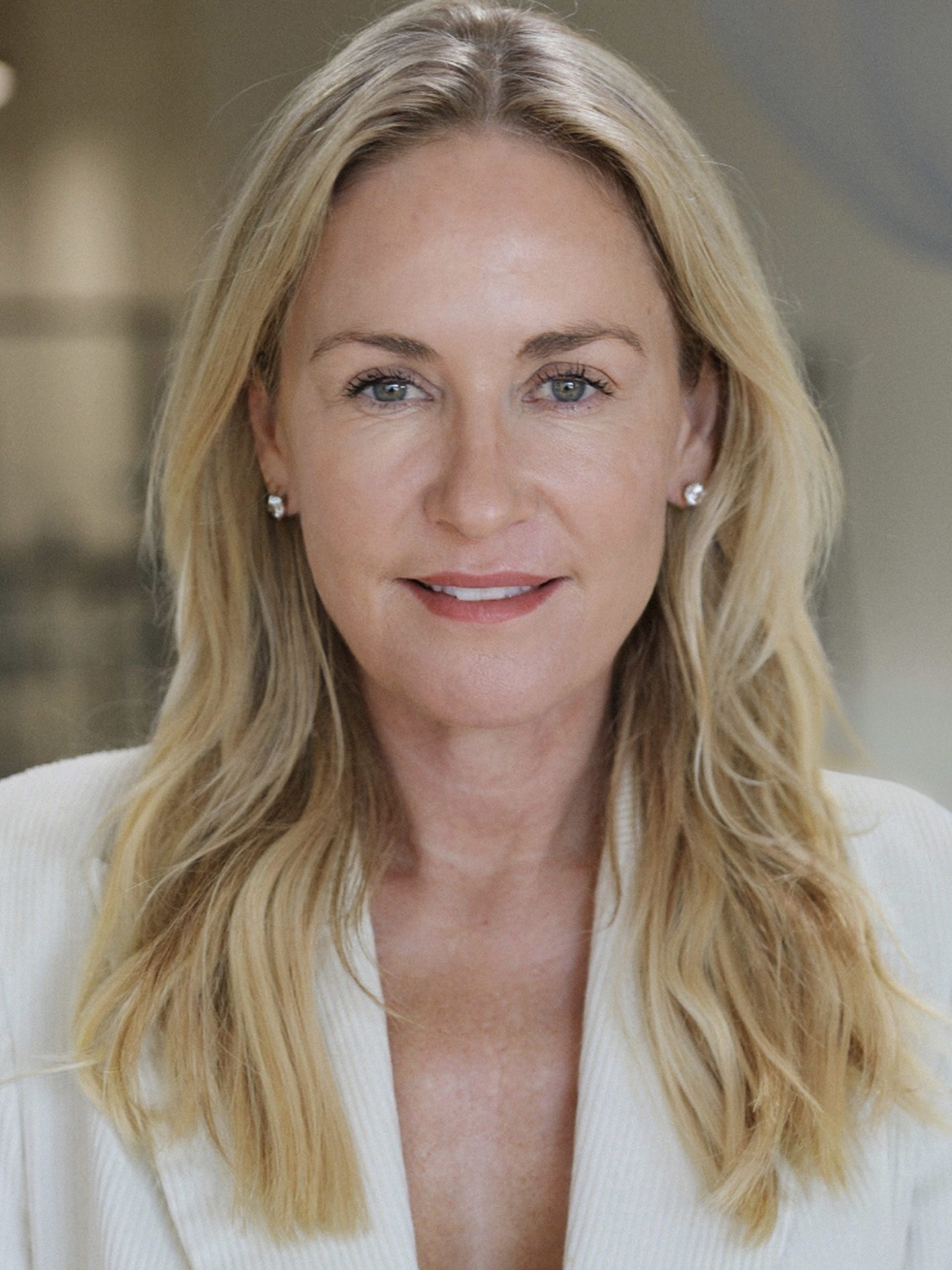 Blonde woman in white top smiling confidently against a soft neutral background.