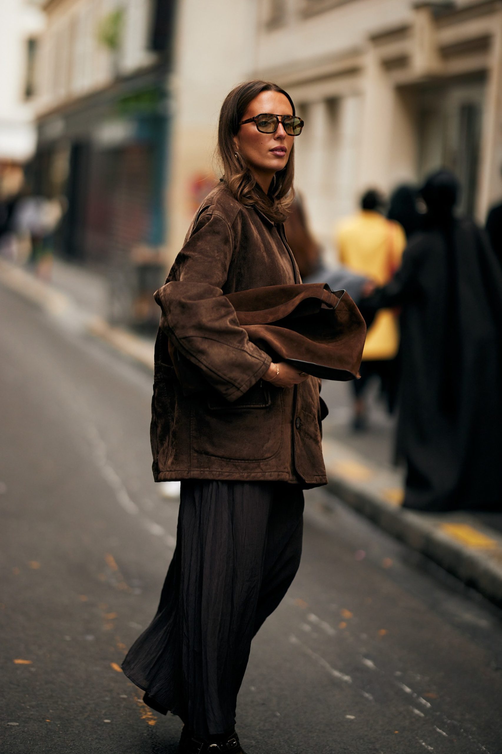 Woman in oversized brown suede jacket and dark maxi skirt walking on a Parisian street.