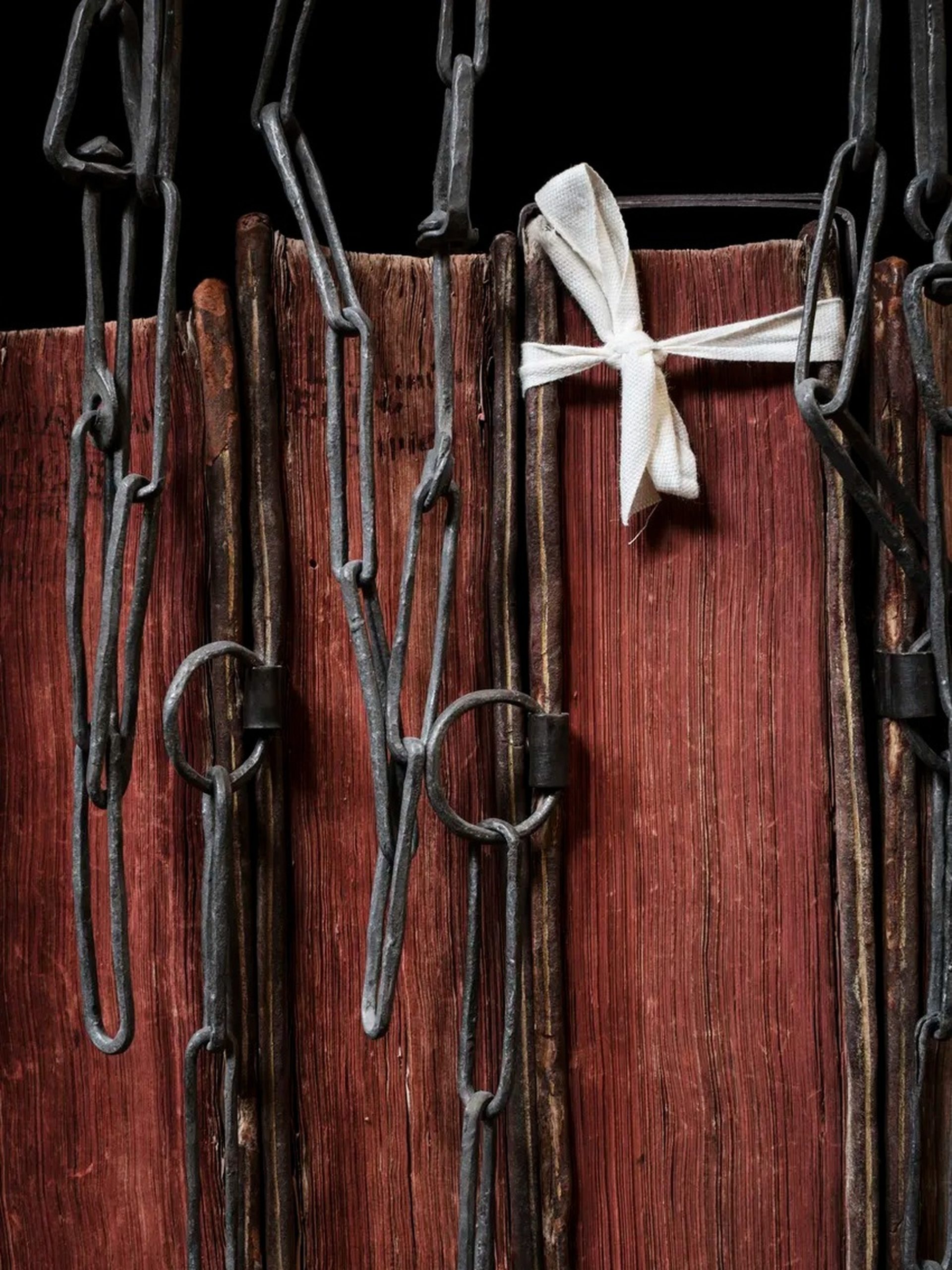 Ancient red-edged books secured with heavy iron chains and a white ribbon bow.