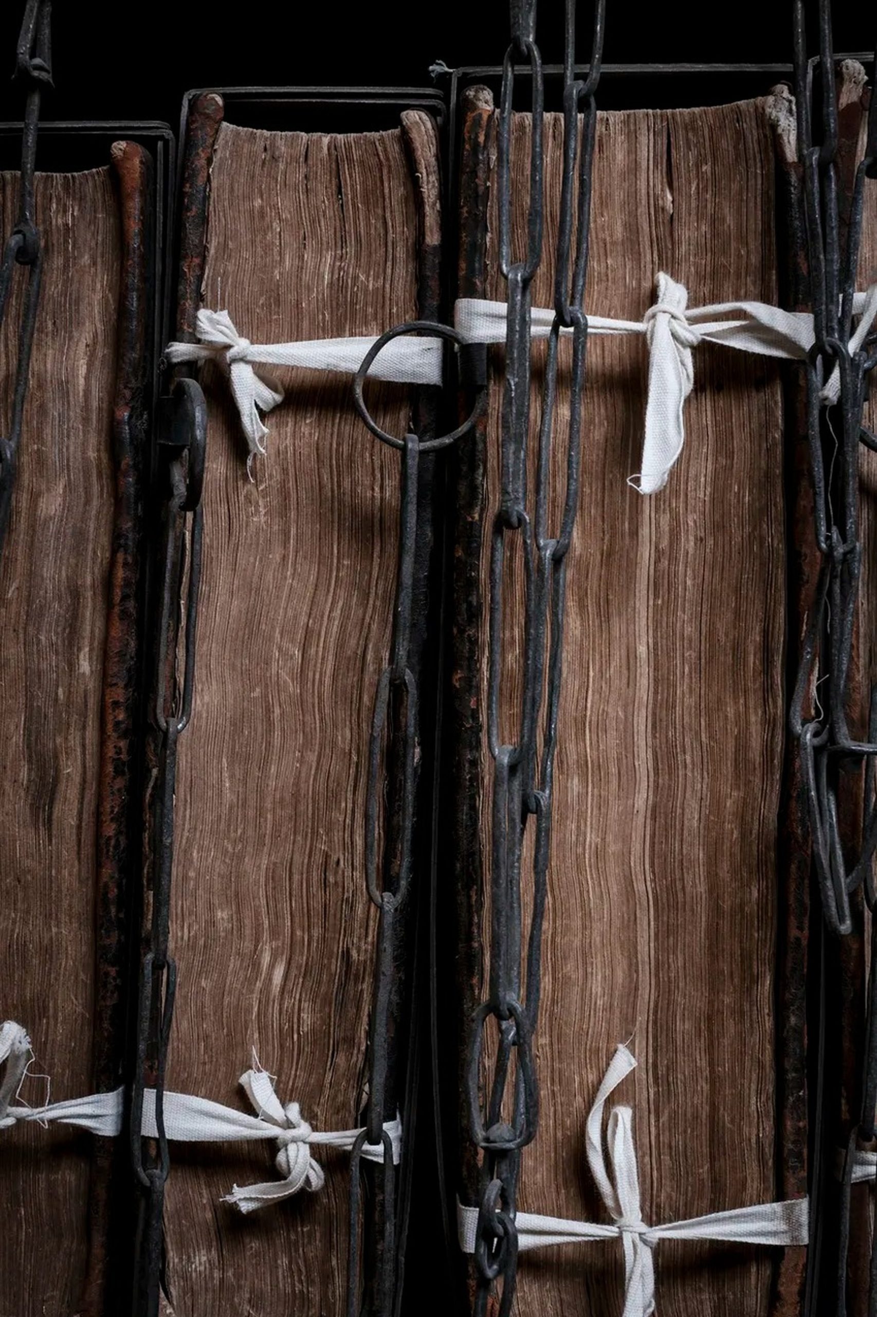 Close-up of ancient weathered books secured with heavy iron chains and white linen ties.