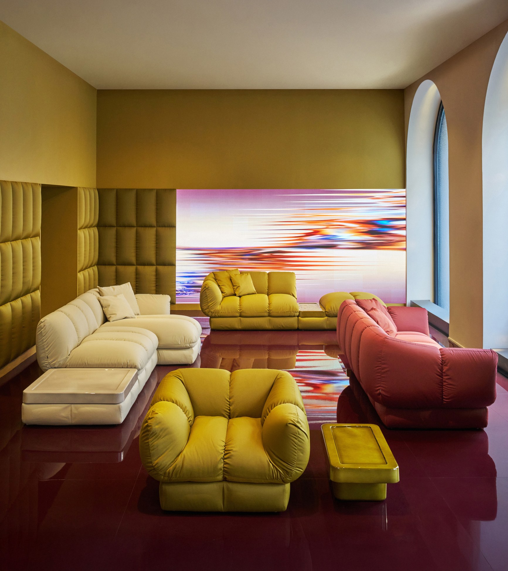 Luxury interior with cream, yellow, and rose-red sofas on a glossy red floor beneath a glowing abstract artwork.
