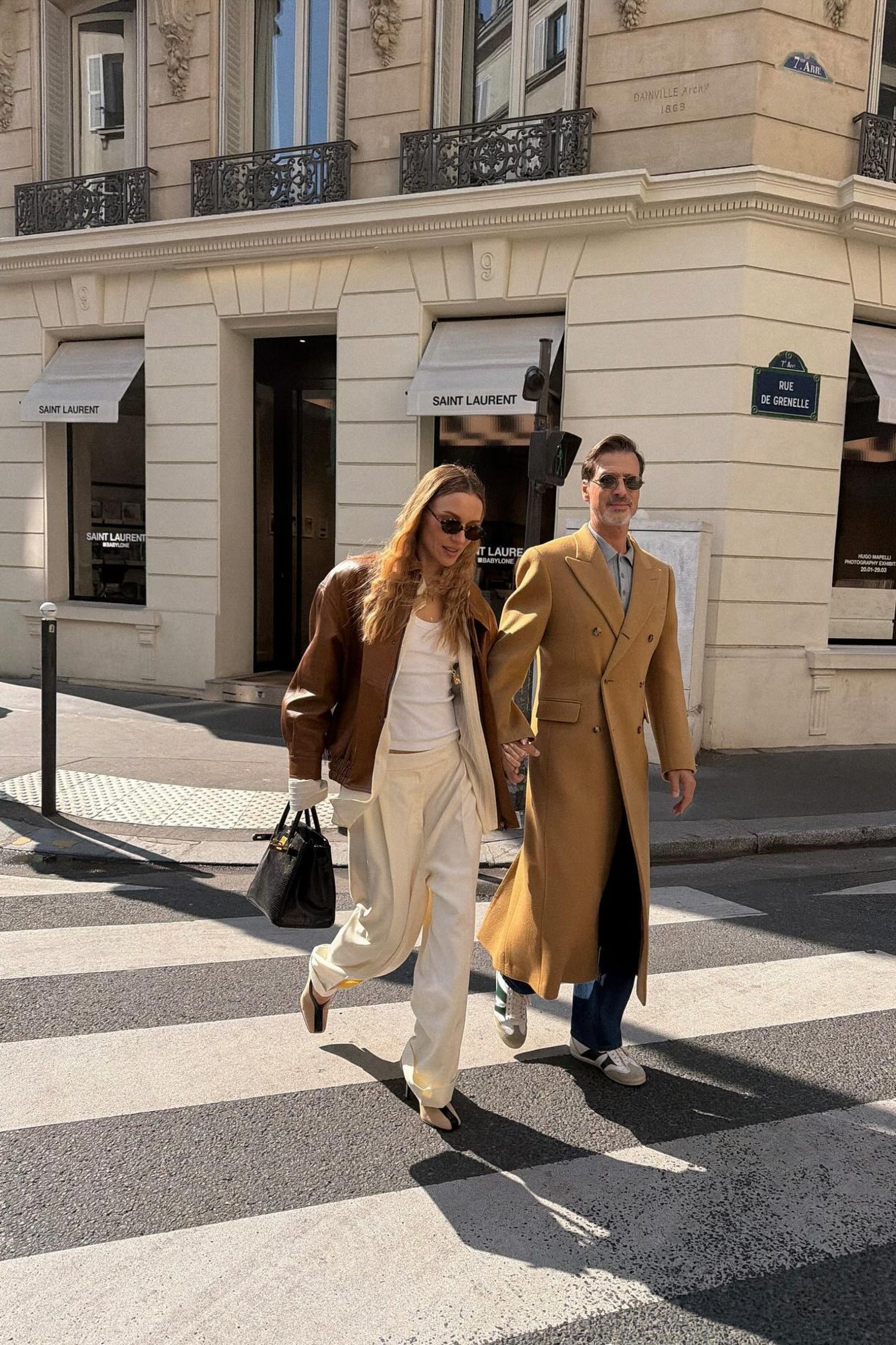 Couple crossing a Paris street outside Saint Laurent on Rue de Grenelle in stylish outfits.