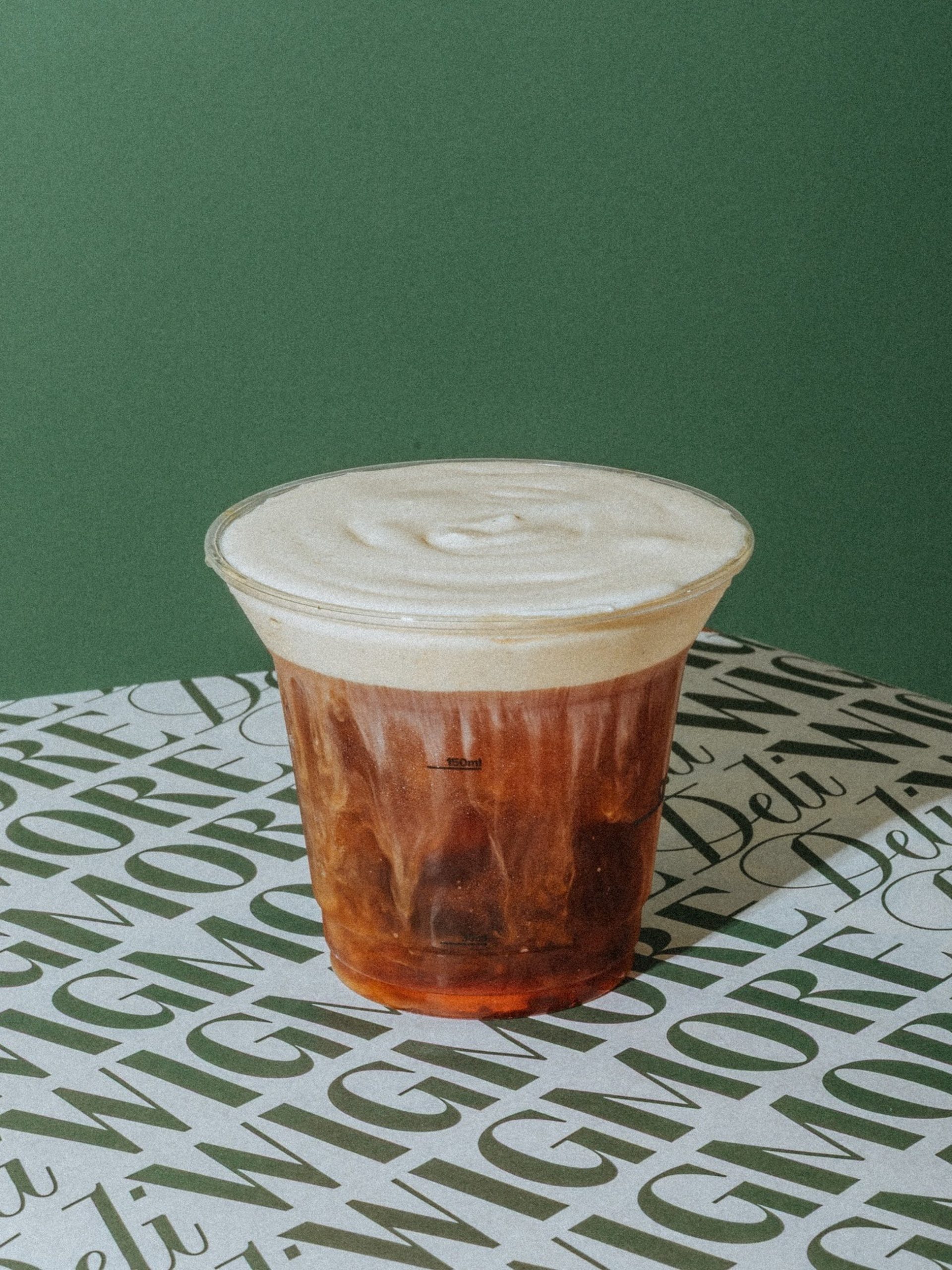 Iced coffee drink with cream foam topping in clear cup on branded Wigmore Deli paper.