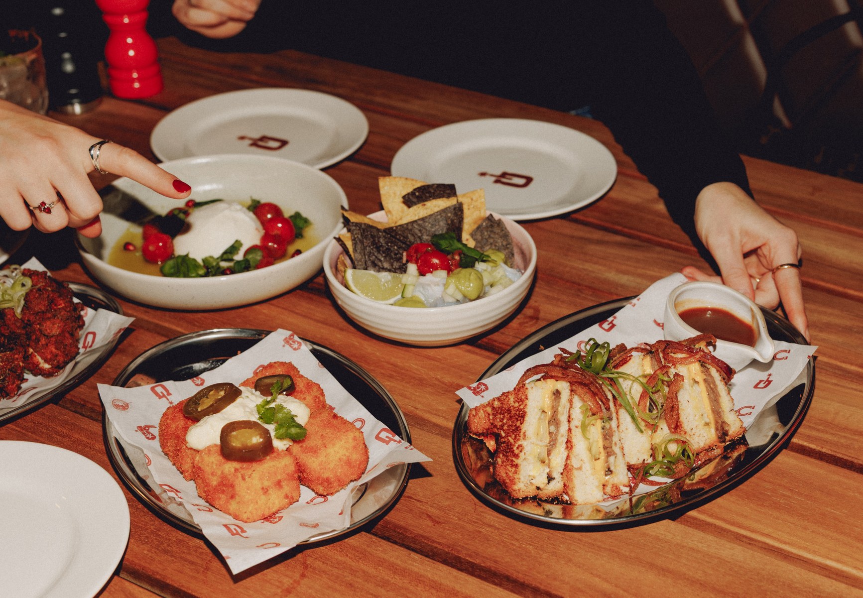 Multiple share plates of fried croquettes, burrata, ceviche, and crumbed sandwich on a restaurant table.
