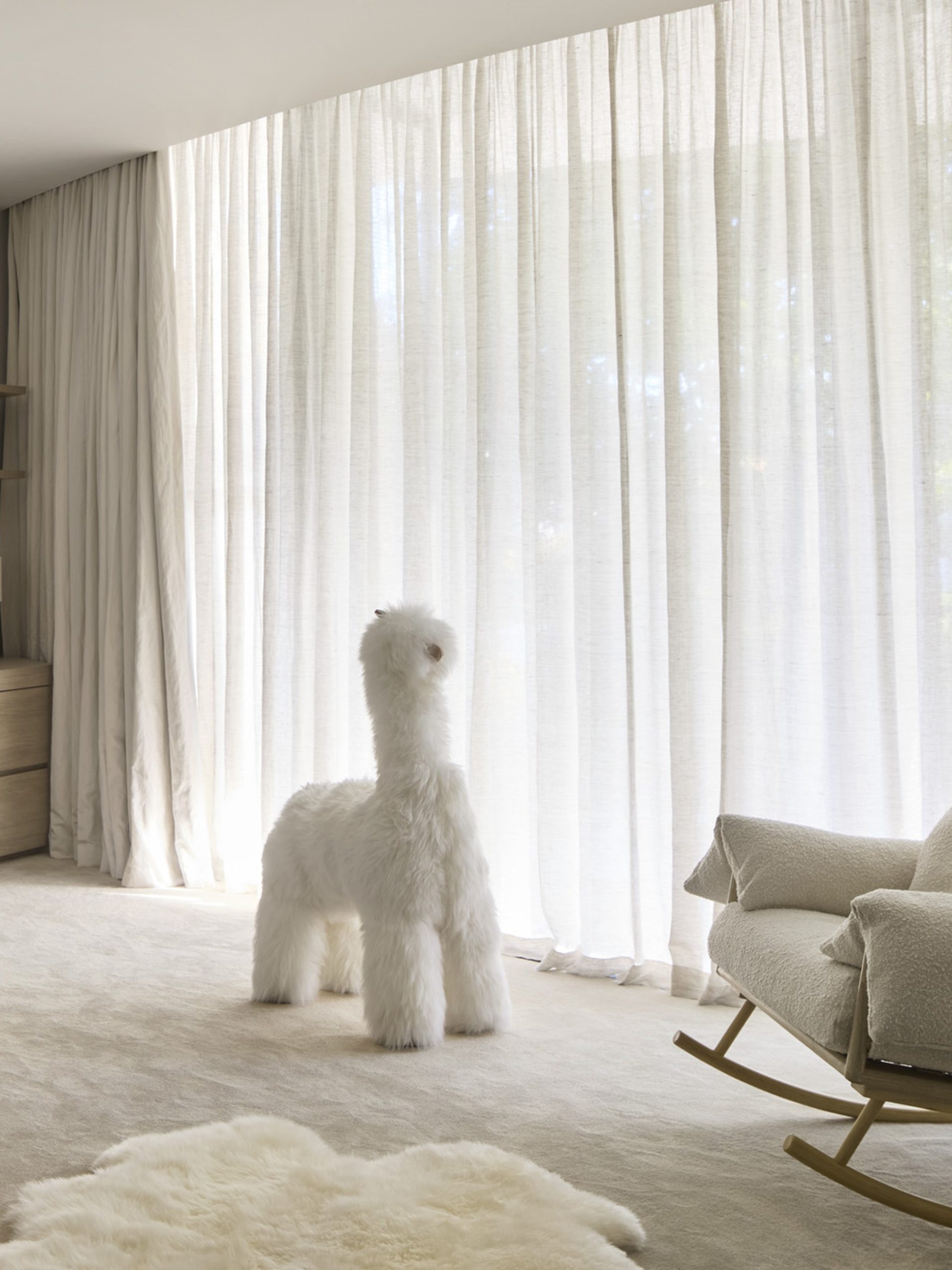 Elegant neutral nursery with oak crib, Hermès blanket, fluffy llama sculpture, and sheer curtains.
