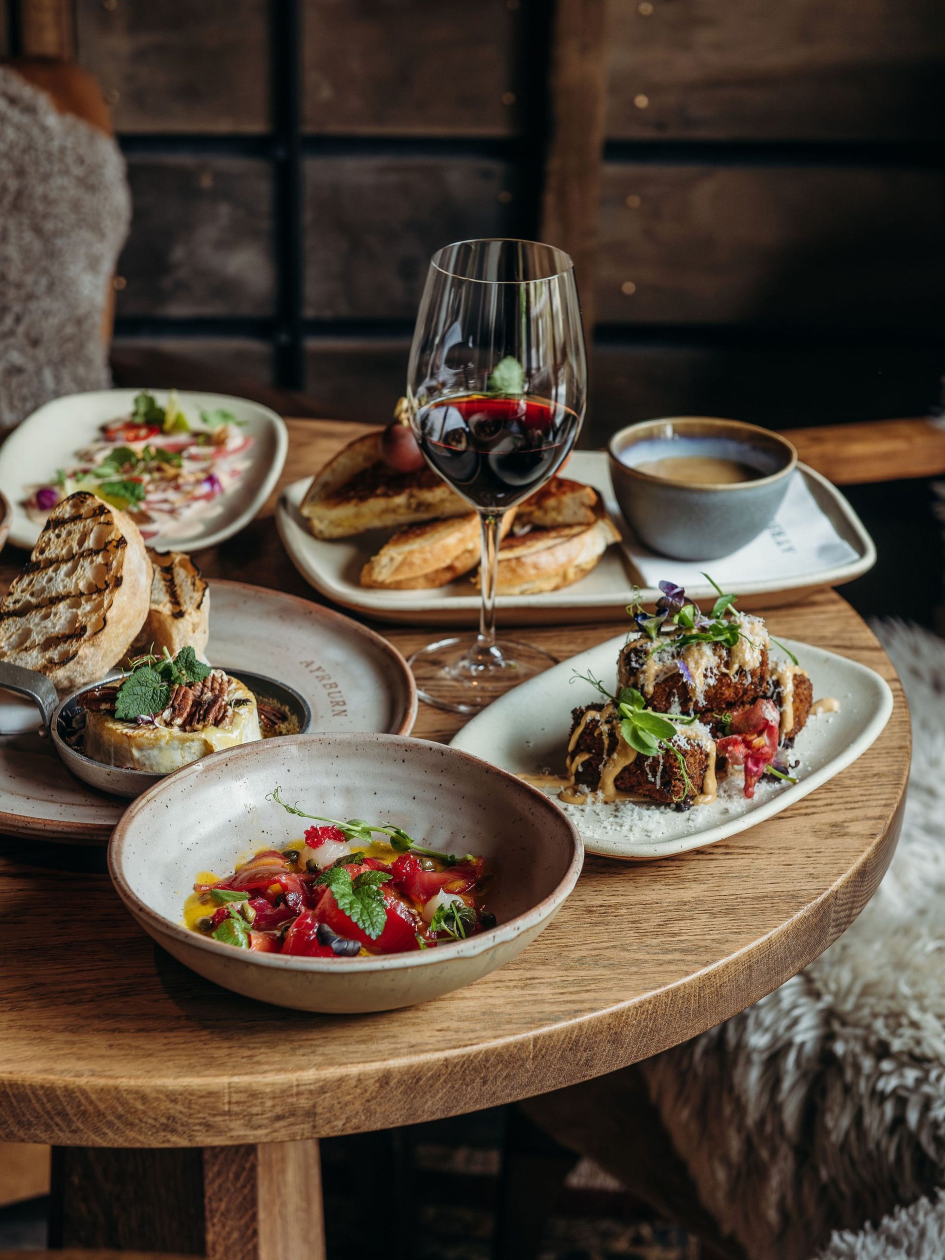 Rustic wooden table set with gourmet share plates, red wine, and coffee in a cosy alpine lodge.