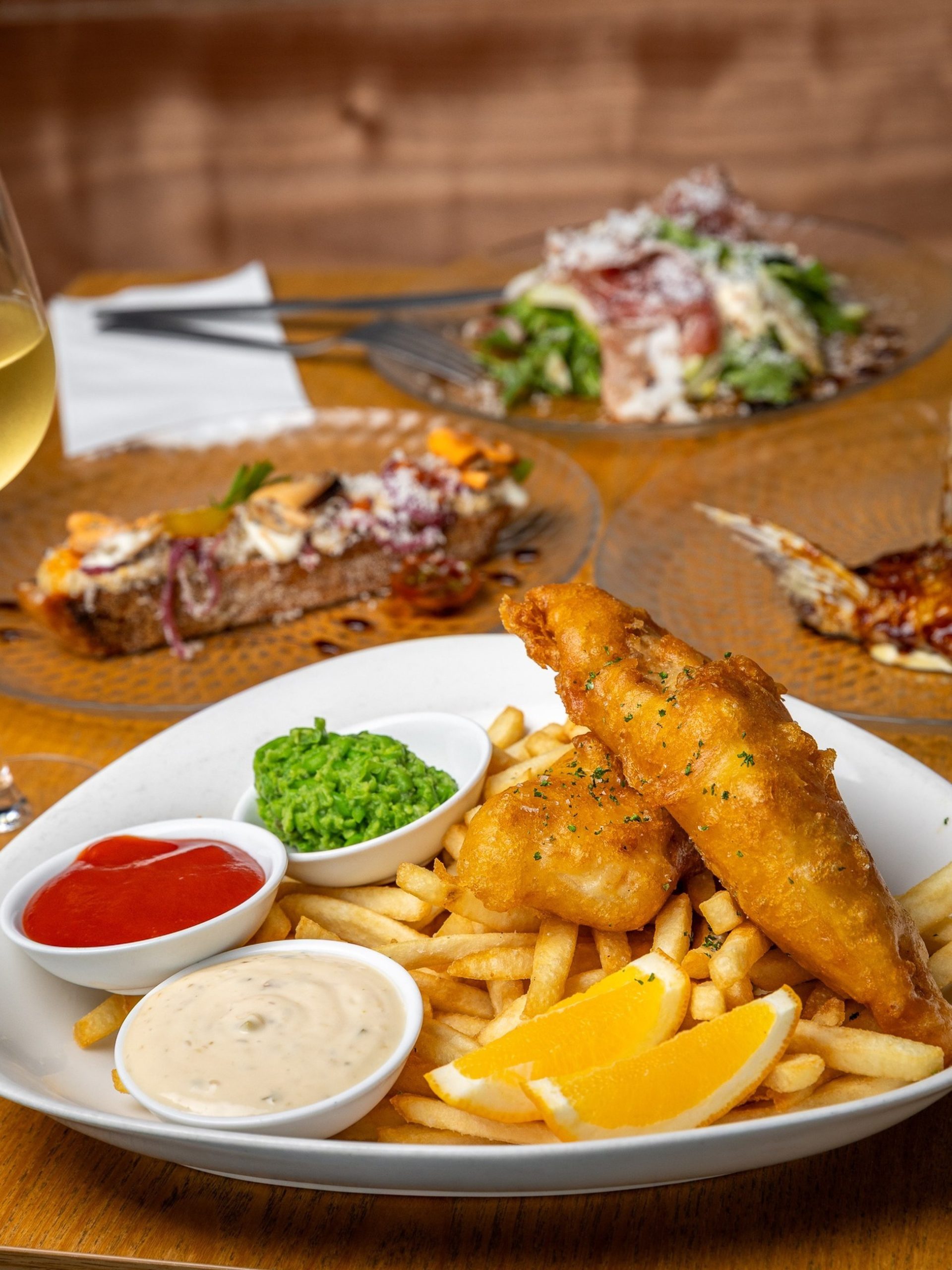 Golden beer-battered fish and chips with mushy peas, tartare sauce, and lemon wedges on a white plate.