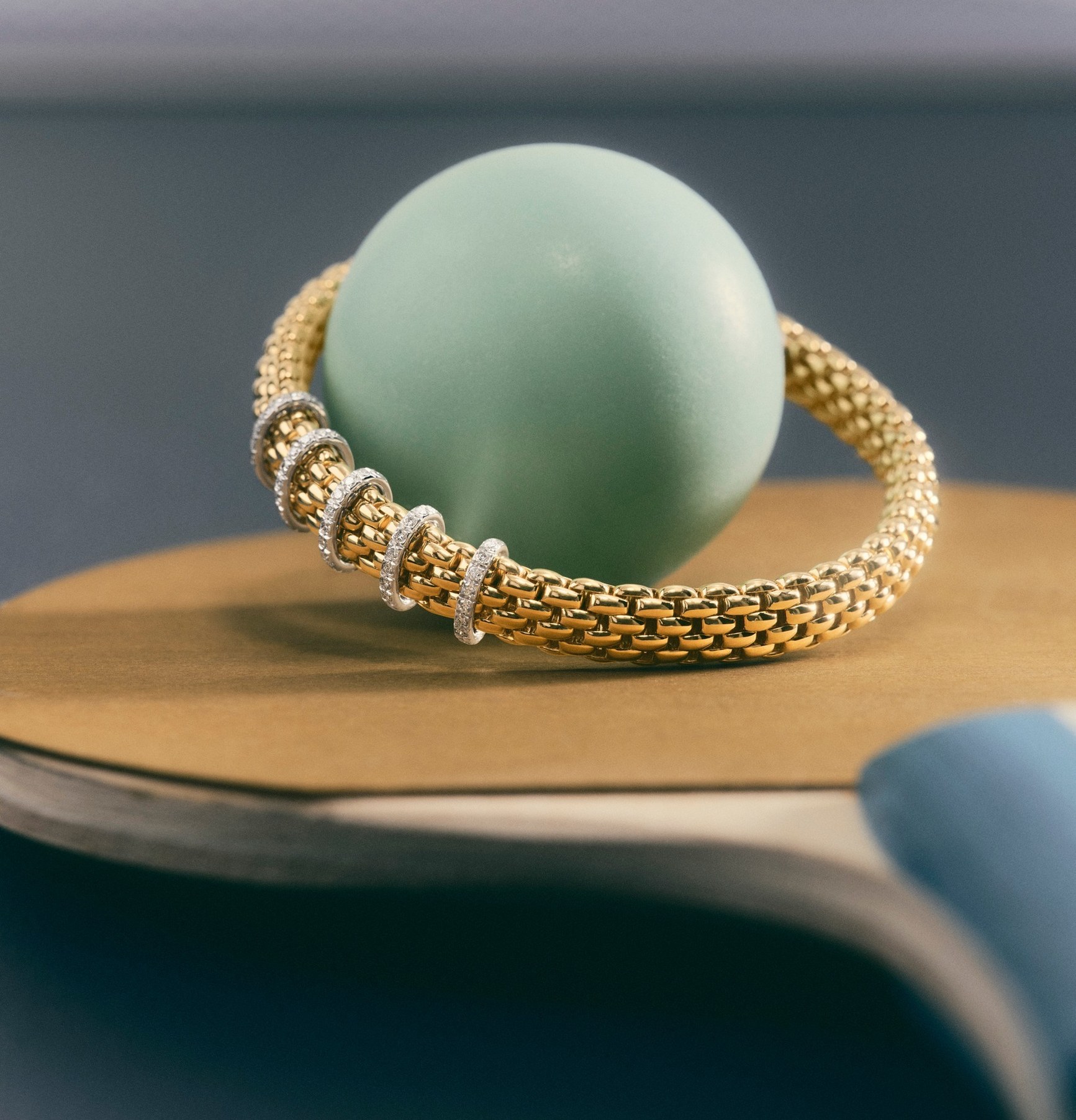 Gold mesh bracelet with diamond rondelles draped around a mint green sphere on a gold disc.