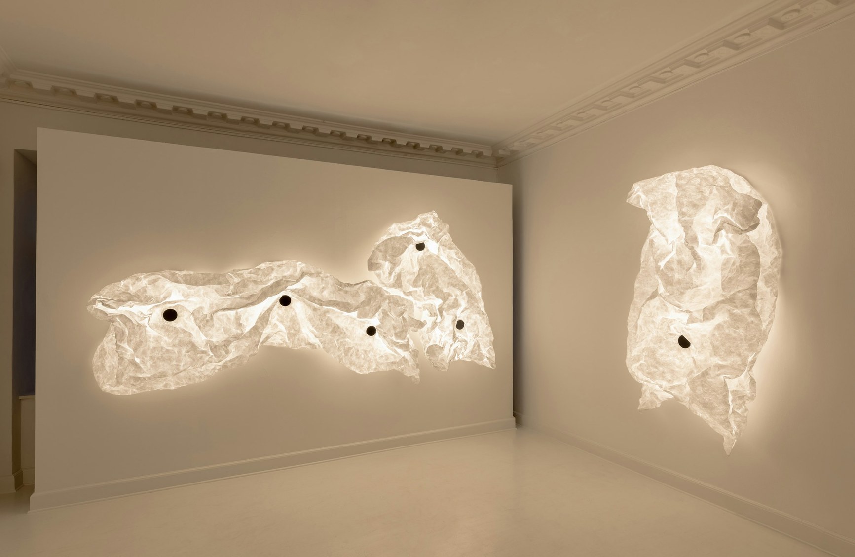 Two large glowing crumpled translucent wall sculptures illuminate a white gallery room.