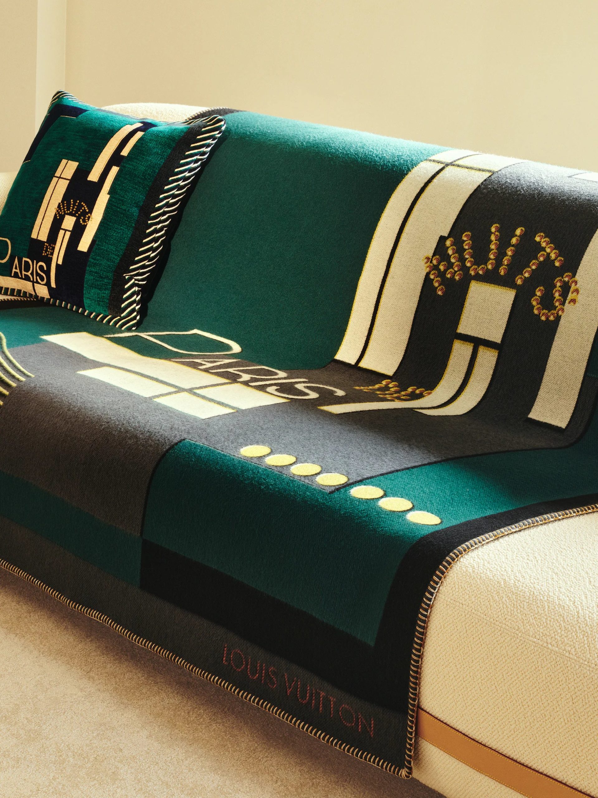 Emerald green Louis Vuitton Paris-motif wool blanket and cushion draped over a cream sofa.