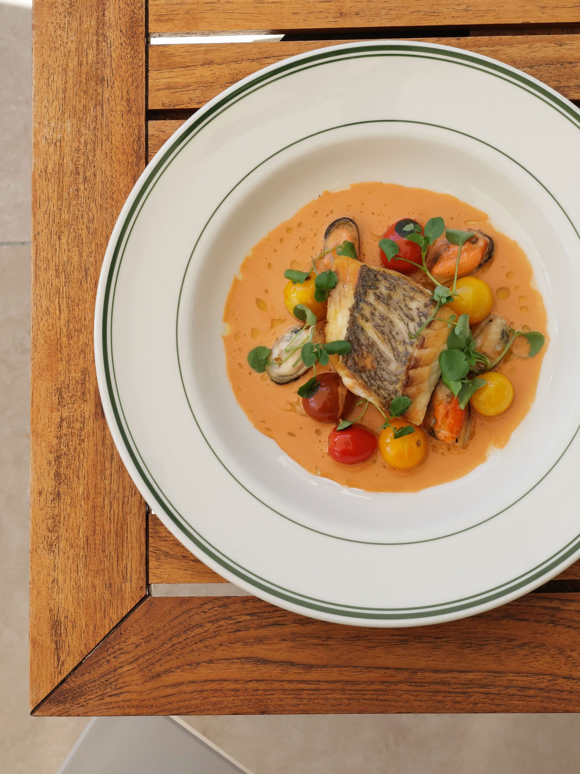 Overhead shot of pan-seared fish fillet with mussels, cherry tomatoes, and bisque sauce in white bowl.