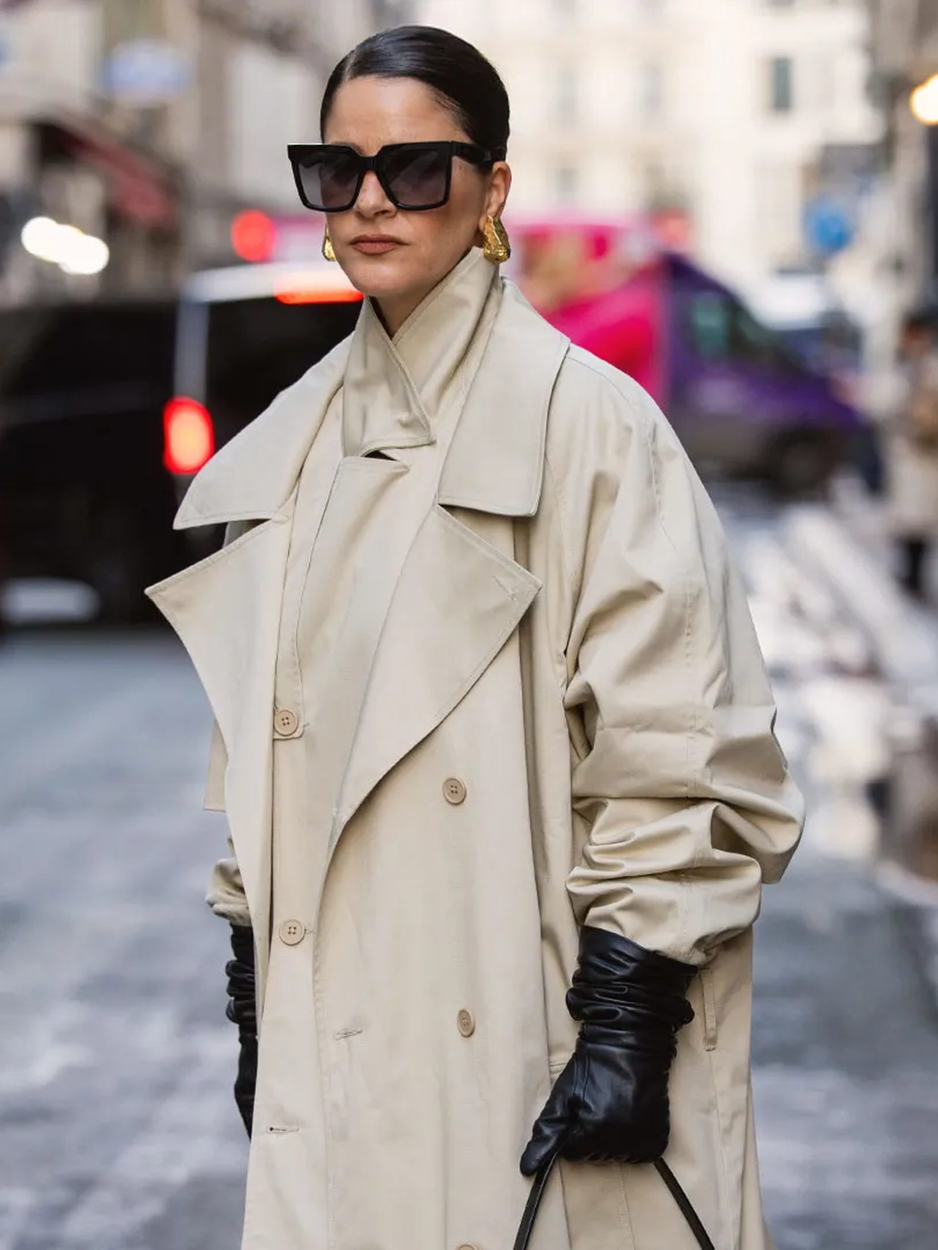 Woman in oversized beige trench coat and black leather gloves posing on a Parisian street.