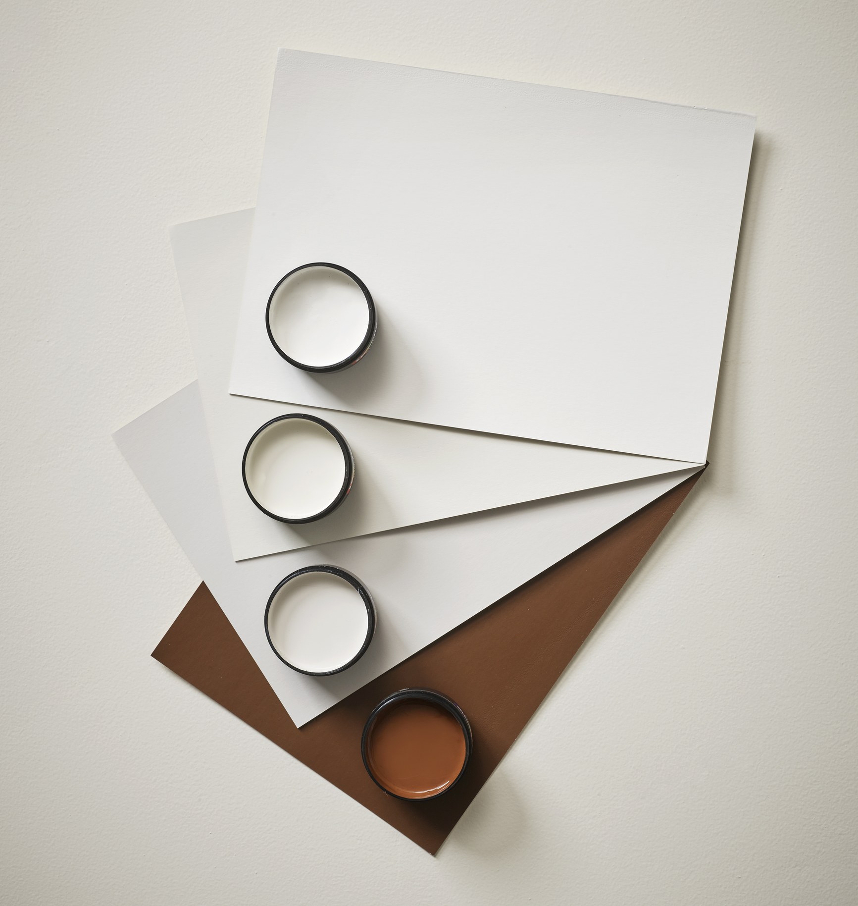 Four Resene paint swatches and sample pots arranged in a gradient from white to terracotta brown.