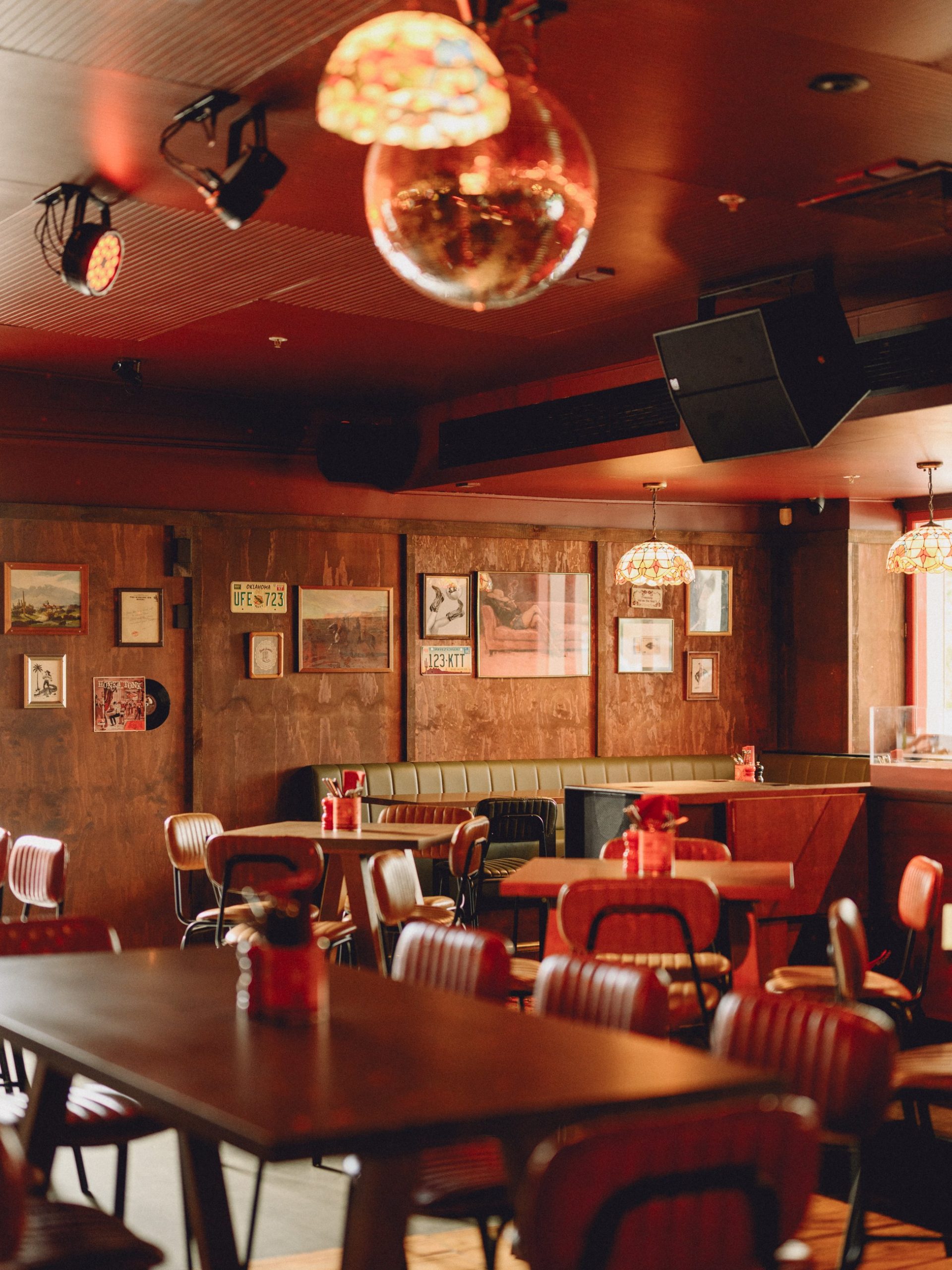 Empty retro bar interior with orange leather chairs, disco ball, and warm pendant lighting.