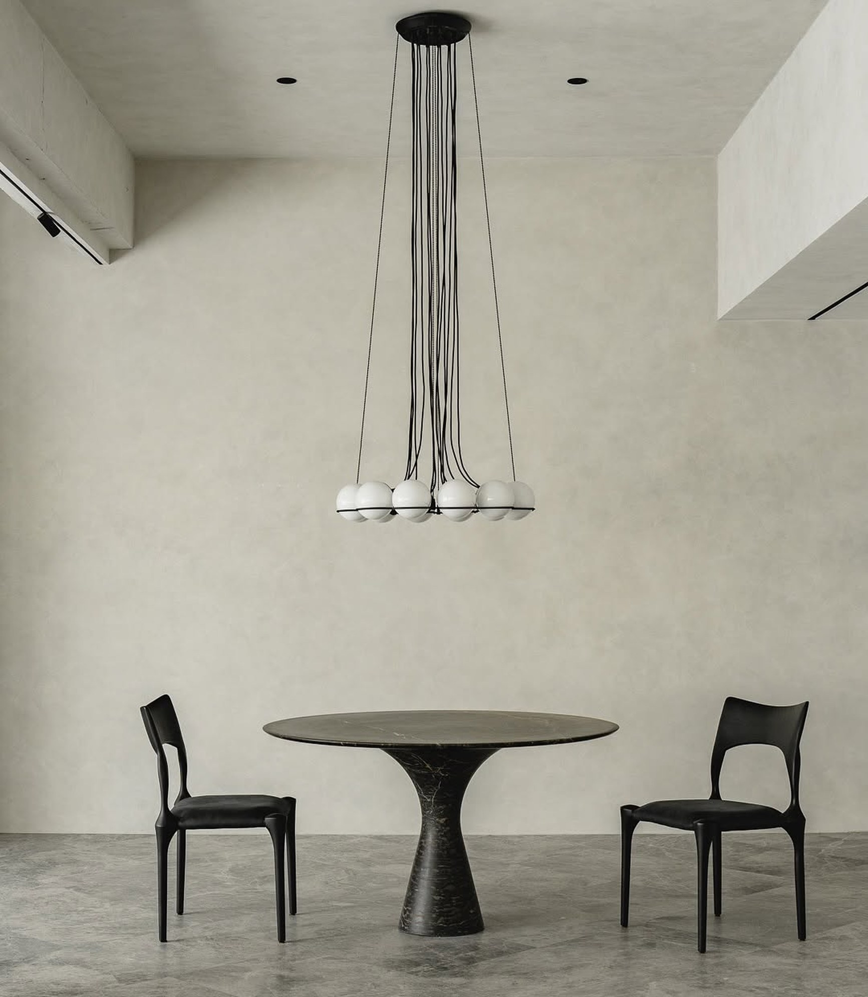 Round black marble dining table with two black leather chairs beneath a globe pendant chandelier.