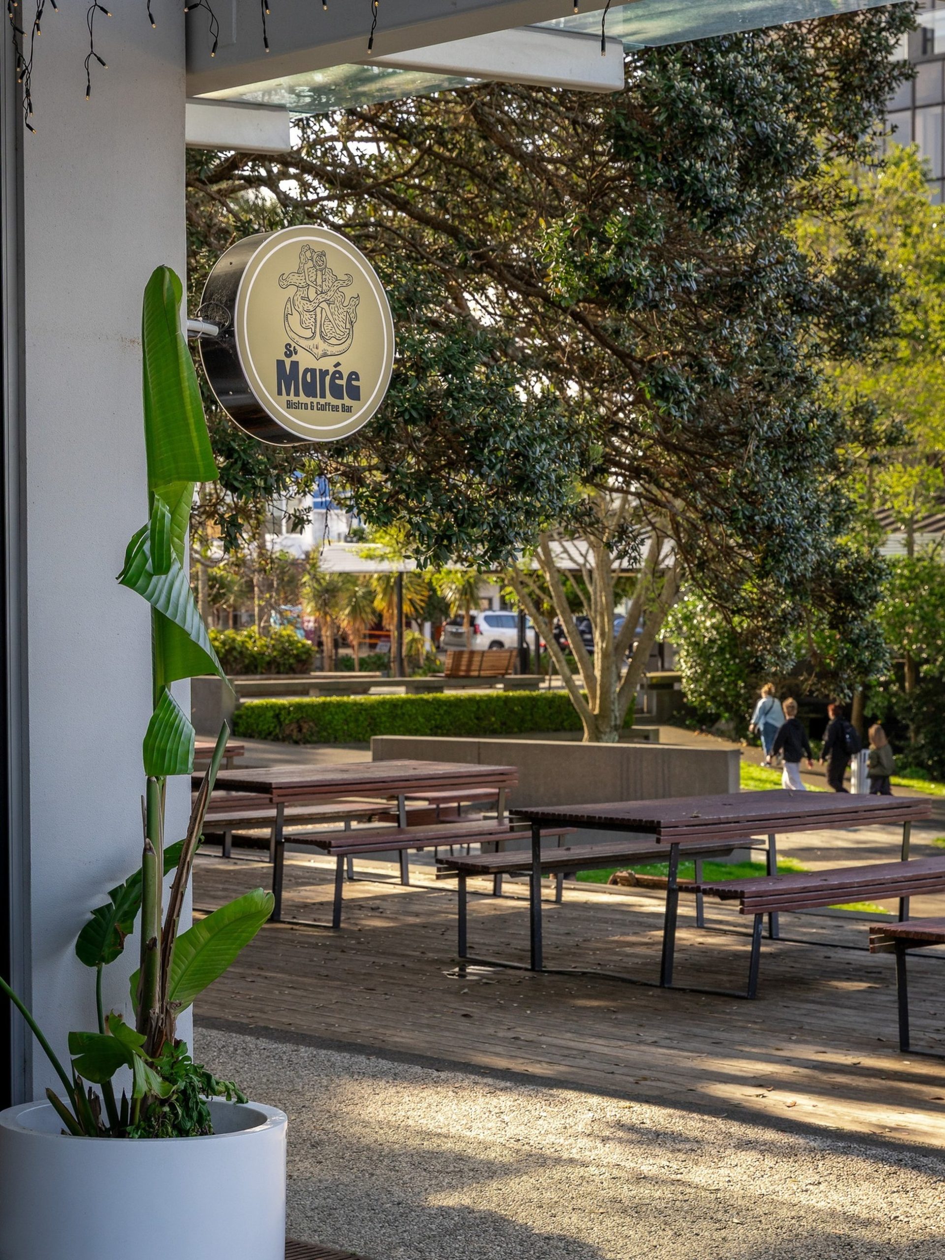Outdoor terrace of St Marée Bistro and Coffee Bar with timber tables, lush trees, and warm sunlight.