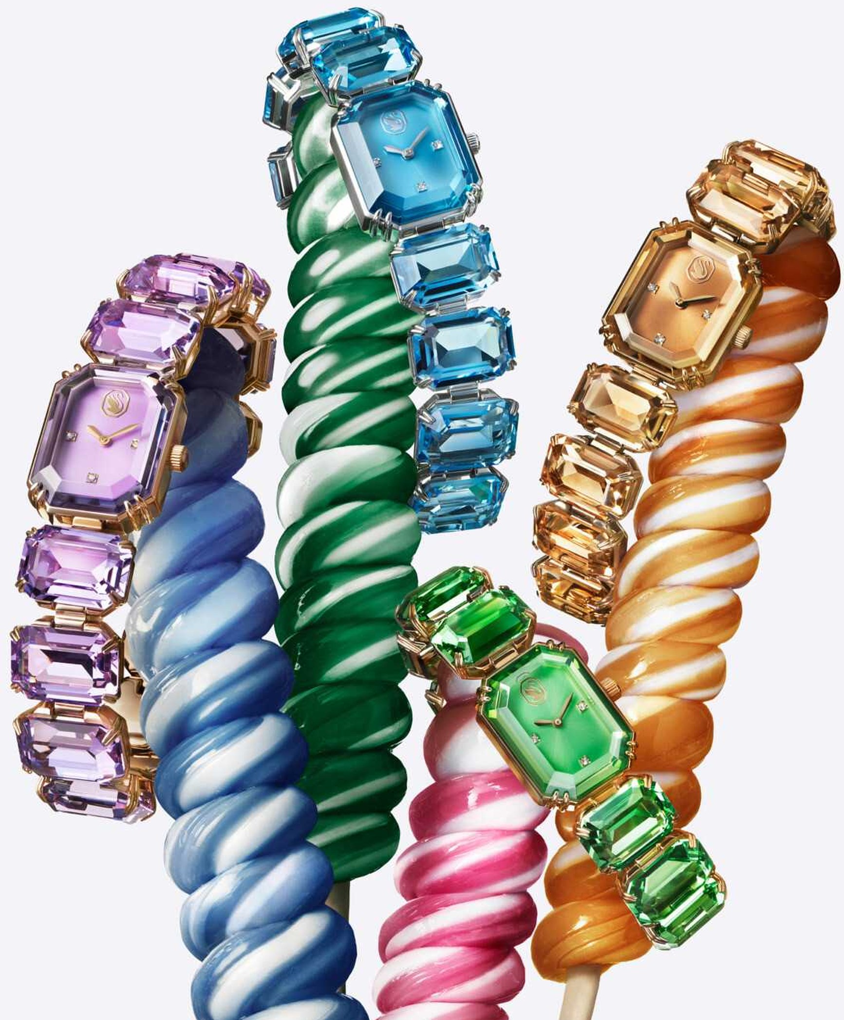 Four colourful Swarovski crystal watches draped over twisted candy lollipop props in blue, green, pink and gold.