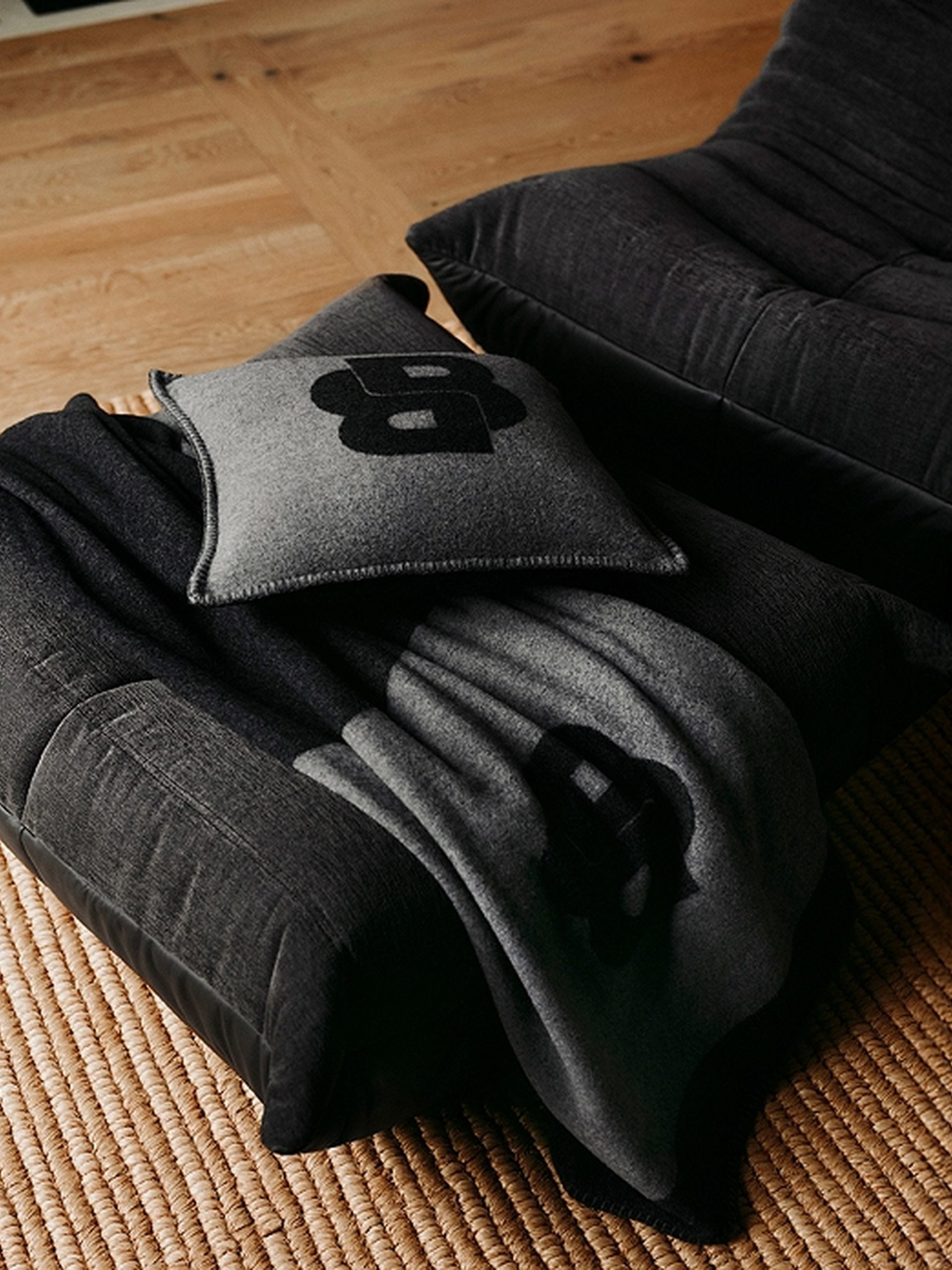 Dark grey modular sofa with folded throw blanket and small cushion on jute rug.