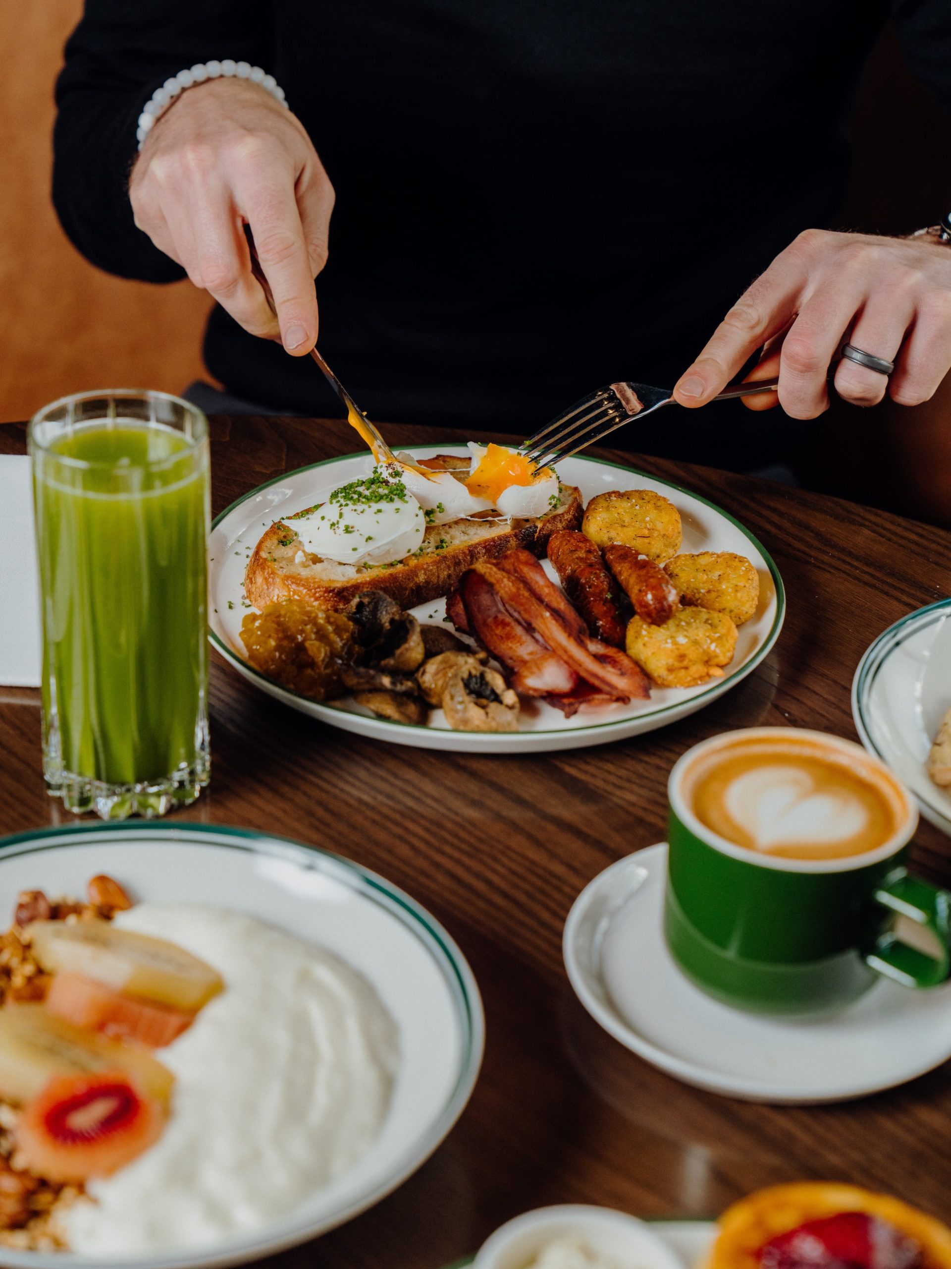 Person cutting into a poached egg on sourdough toast with a full café breakfast spread.