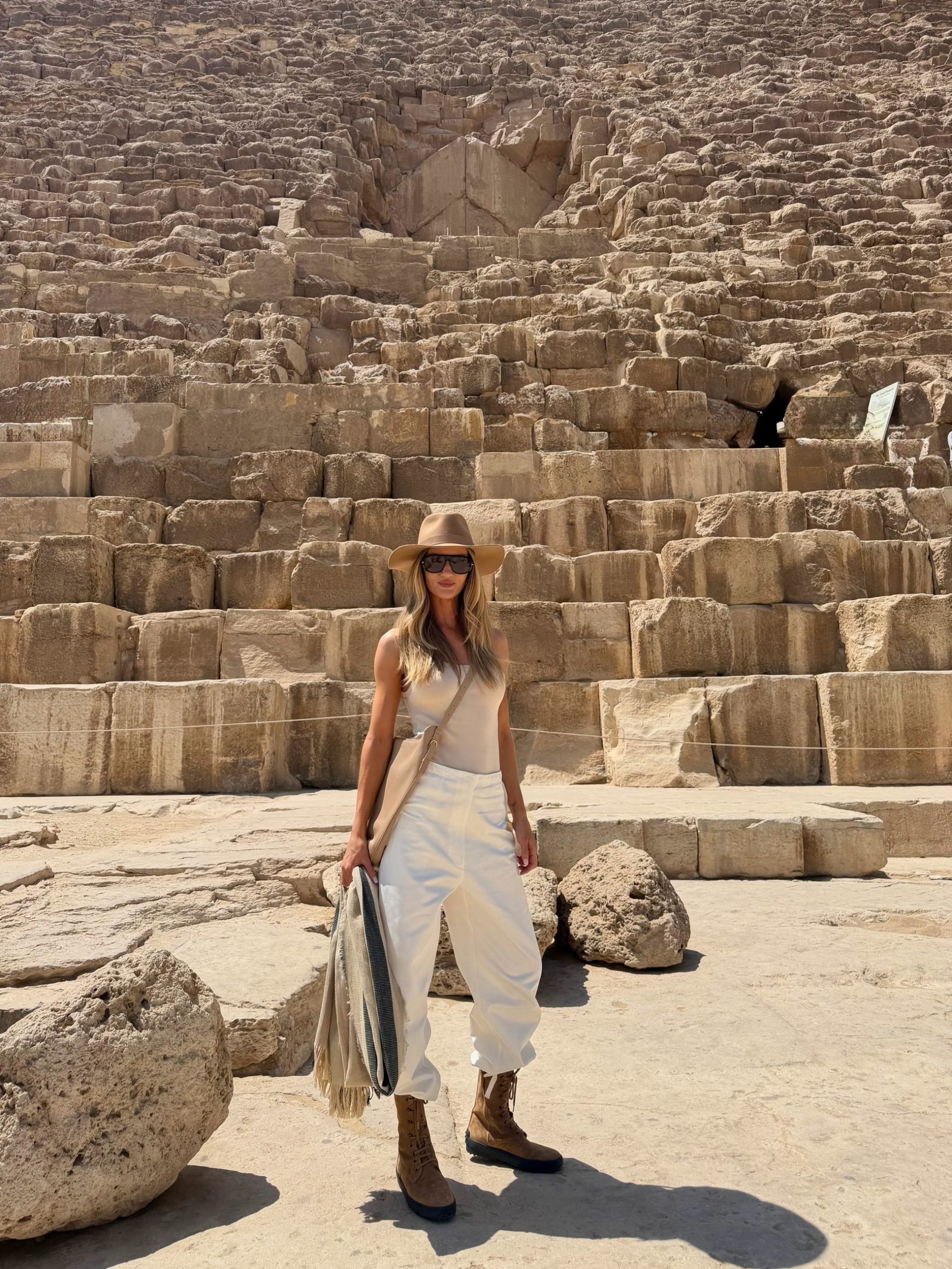 Stylish woman in cream outfit and tan fedora posing before the Great Pyramid of Giza, Egypt.