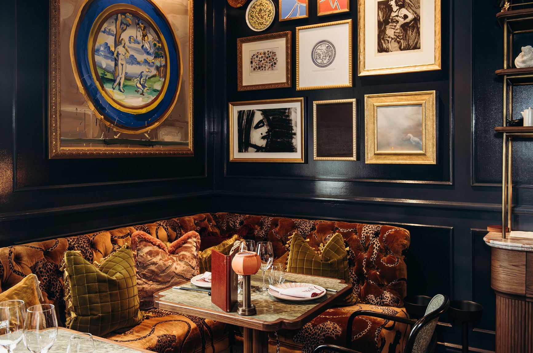 Tufted leopard-print velvet banquette in a dark, art-lined restaurant dining room with marble table.