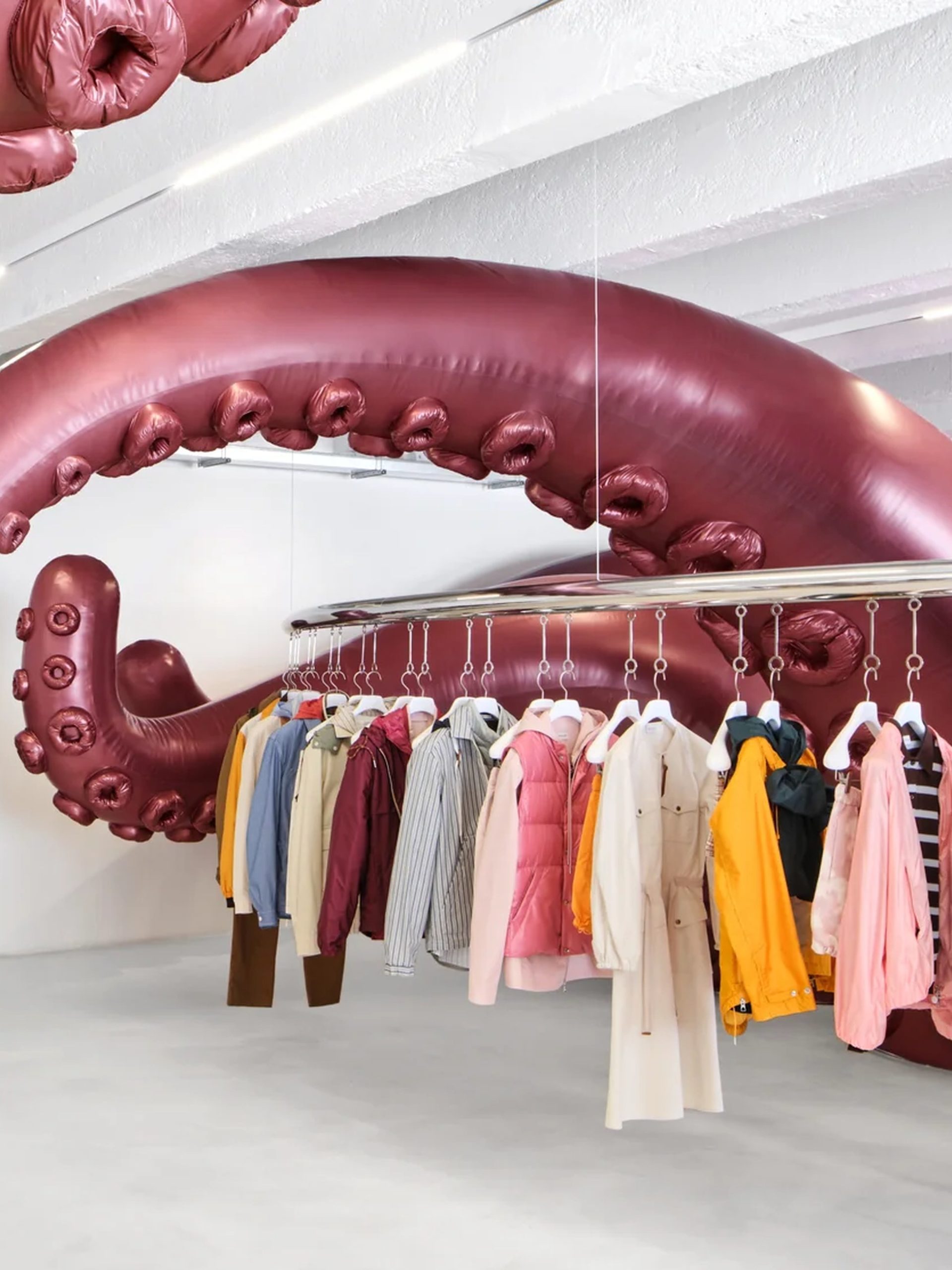 Giant inflatable octopus tentacles suspended above a circular clothing rail in a white gallery-style retail space.