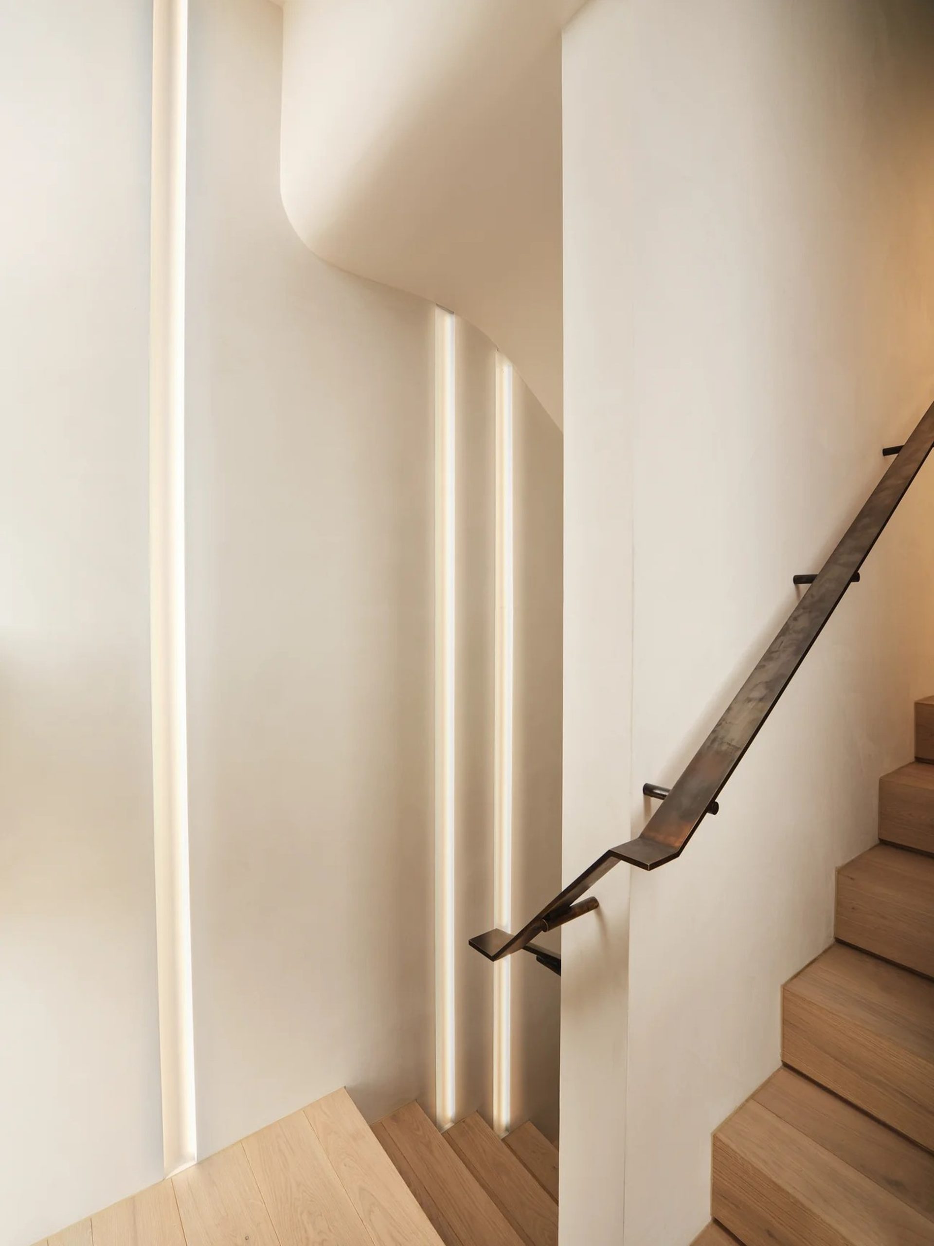 Minimalist staircase with oak treads, recessed LED wall lighting, and a dark forged metal handrail.
