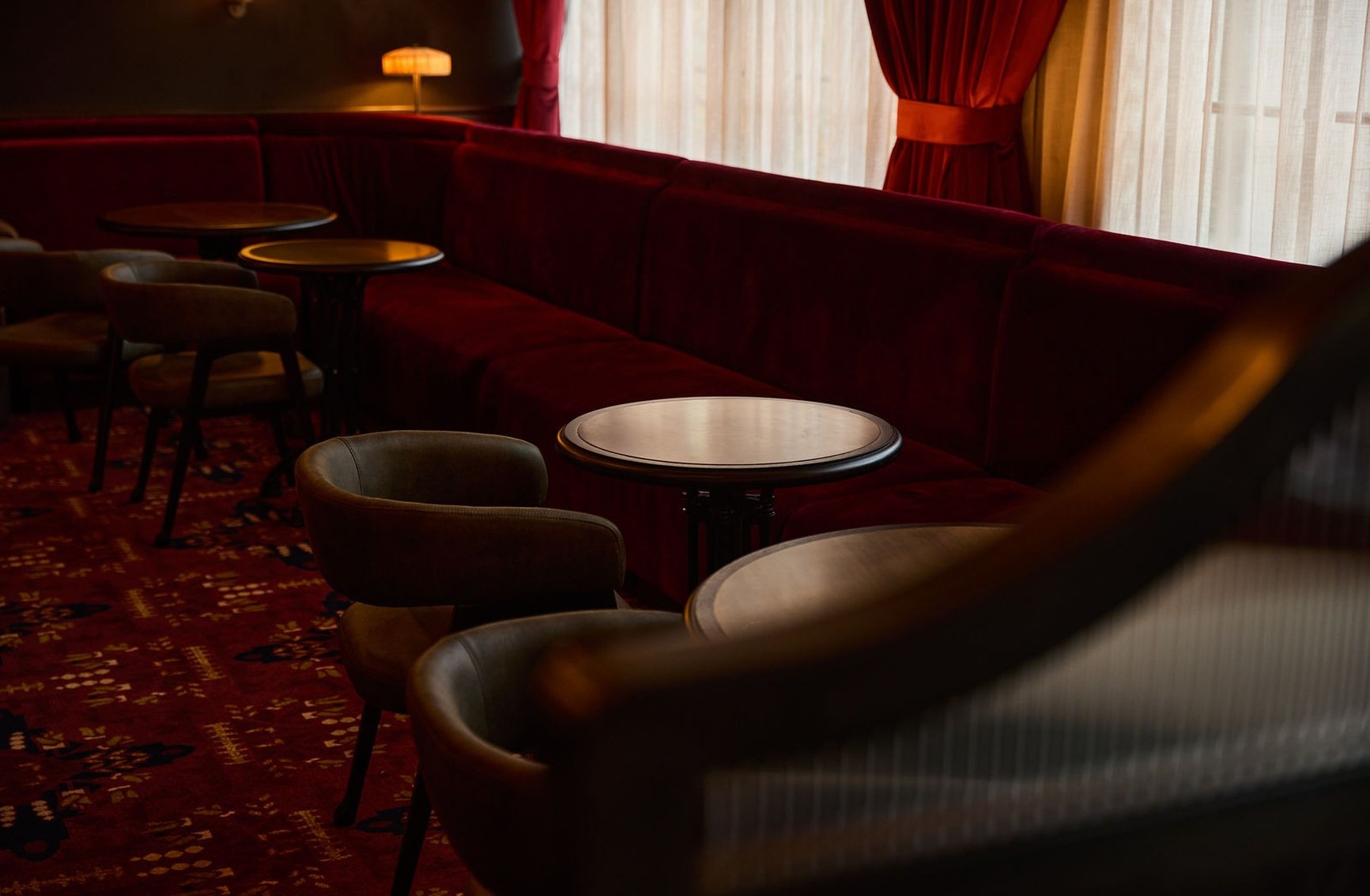 Curved crimson velvet banquette seating with leather armchairs and round tables inside The Halligan bar.