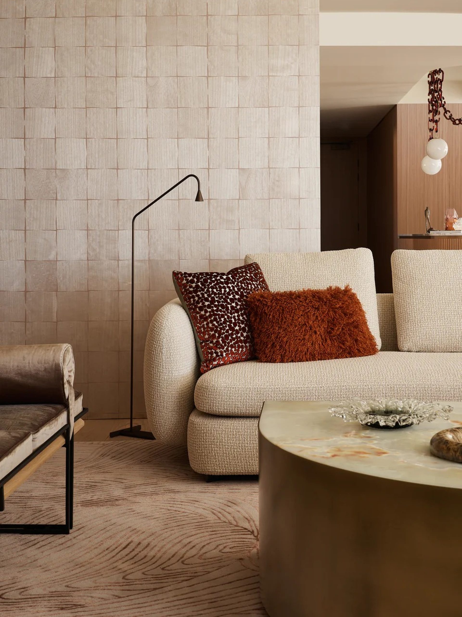 Cream bouclé sofa with rust cushions beside a black arc lamp in a warm, textured living room.