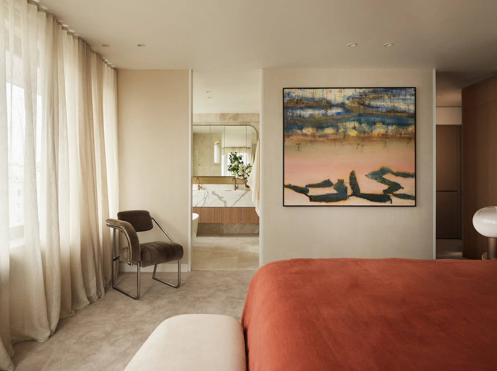 Luxury master bedroom with terracotta bedding, abstract artwork, and marble ensuite visible through doorway.