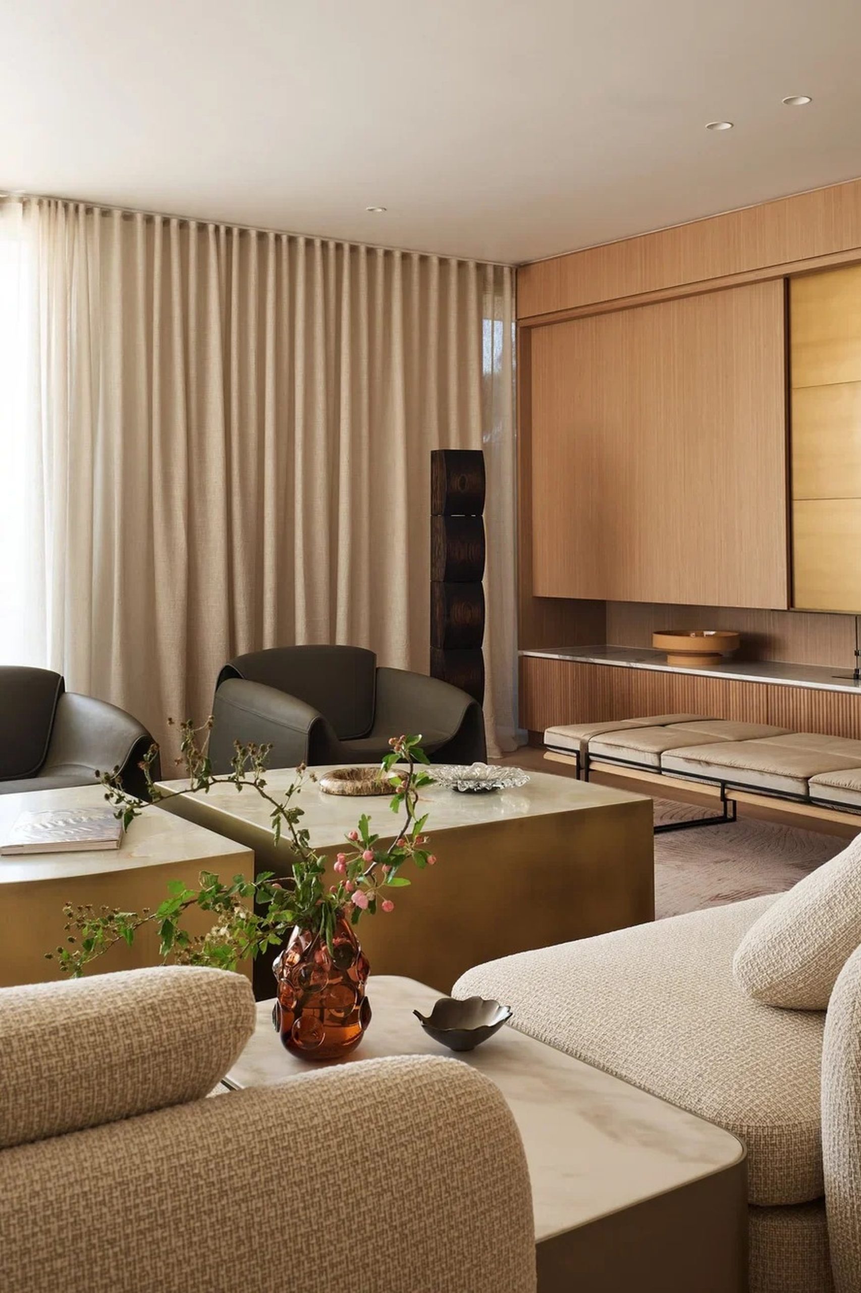 Luxury living room with bouclé sofas, brass coffee table, oak cabinetry, and linen curtains.