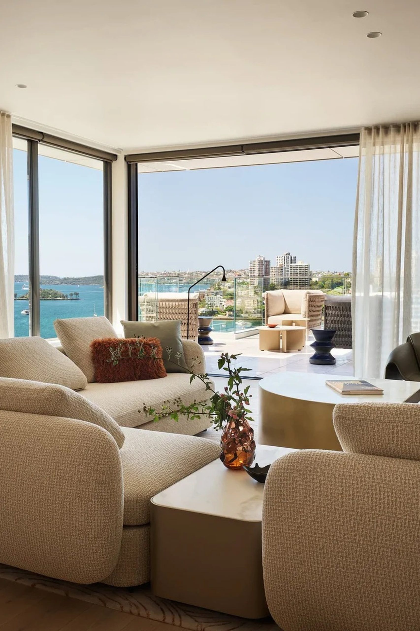 Cream boucle living room with floor-to-ceiling windows overlooking a blue harbour and city skyline.